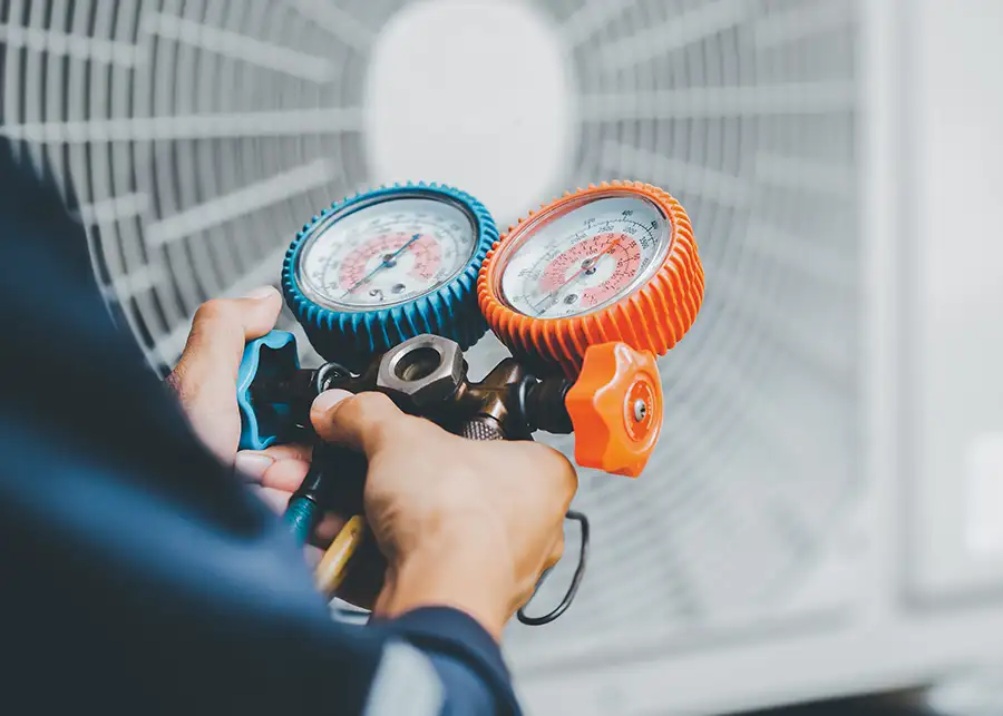 A Precision Climate Control technician holds refrigerant manifold gauges in front of an outdoor AC condenser unit in St. Charles, MO