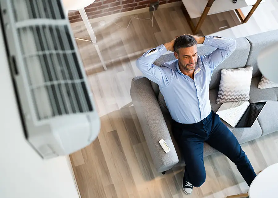 A relaxed man leans back on his couch enjoying cool air from a ductless mini-split system installed by Precision Climate Control in St. Charles, MO - concept of comfort and energy efficiency