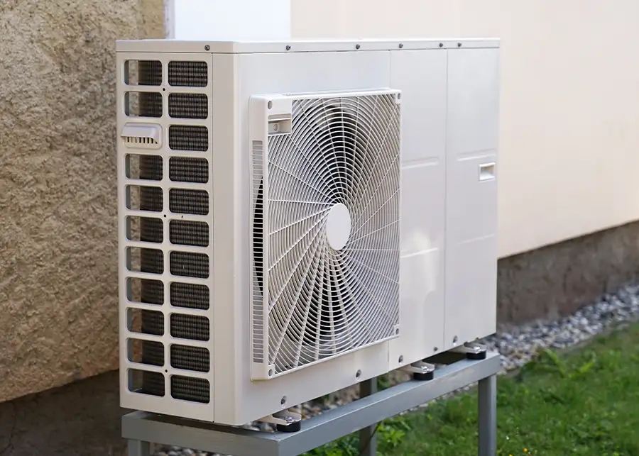 A clean white heat pump outdoor unit mounted on a metal stand against a stucco wall, representing Precision Climate Control's installation services in St. Charles, MO