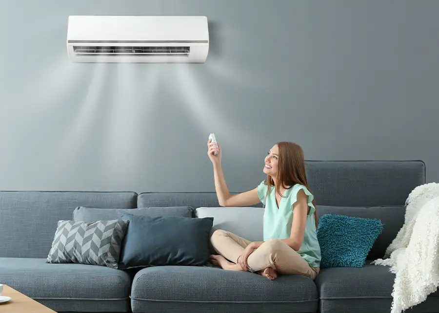 A smiling woman uses a remote control to adjust her wall-mounted ductless mini-split air conditioner, installed by Precision Climate Control in St. Charles, MO
