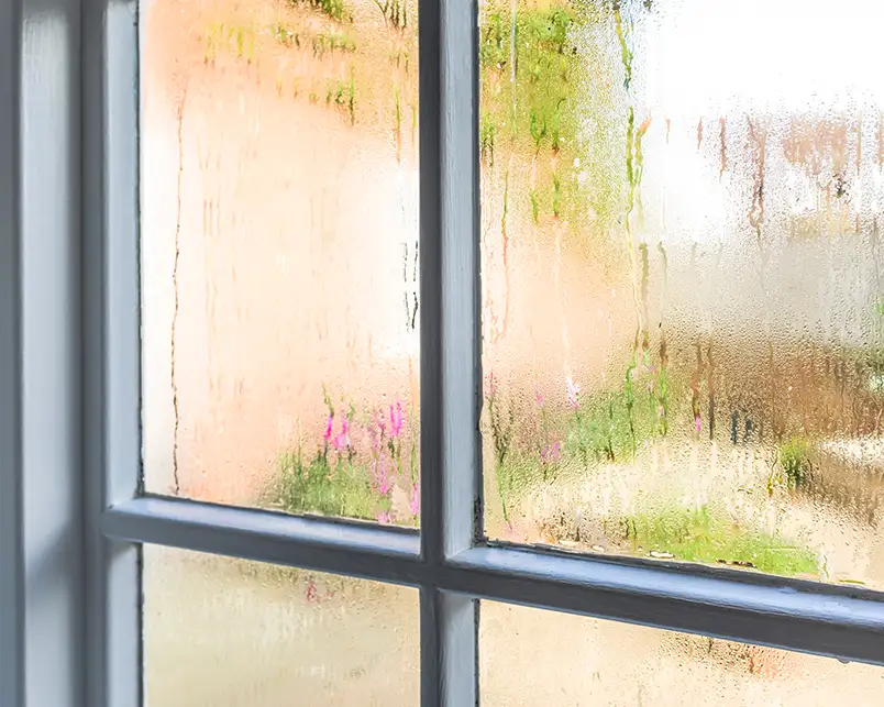 Heavy condensation streaks down a window pane surrounded by a gray frame, highlighting humidity and indoor air quality issues that Precision Climate Control addresses in St. Charles, MO