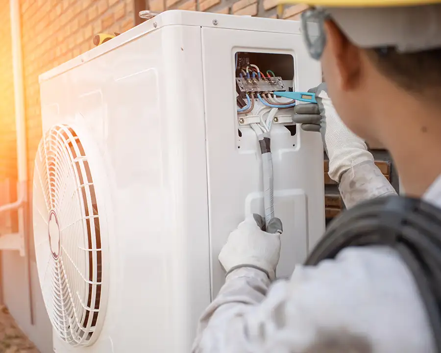 A Precision Climate Control technician in white gloves repairing electrical wiring into the back panel of a heat pump in St. Charles, MO