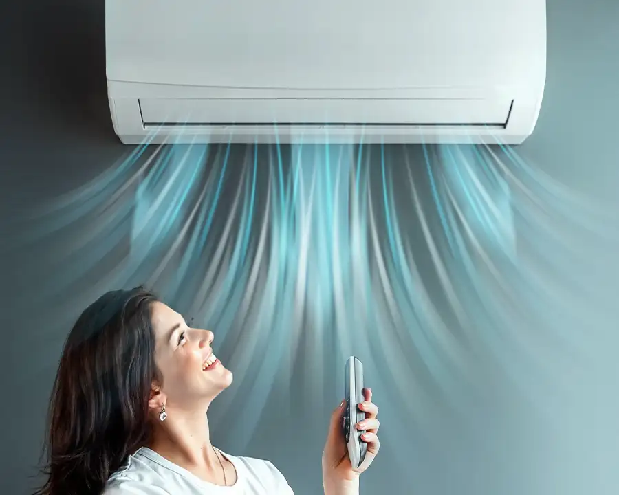 A smiling woman holds a remote and gazes up at a wall-mounted ductless mini-split blowing illustrated blue cool air streams, representing Precision Climate Control's mini-split installation services in St. Charles, MO