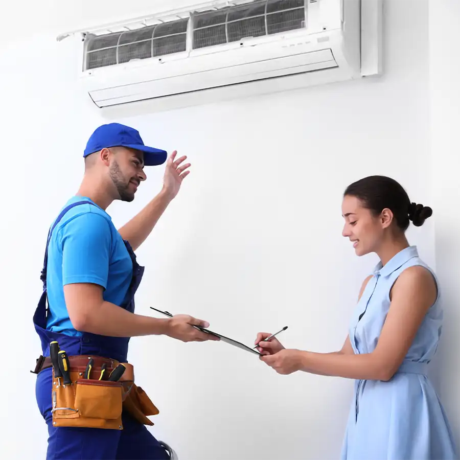 A Precision Climate Control technician in blue overalls and a tool belt explains a completed mini-split installation to a homeowner in St. Charles, MO