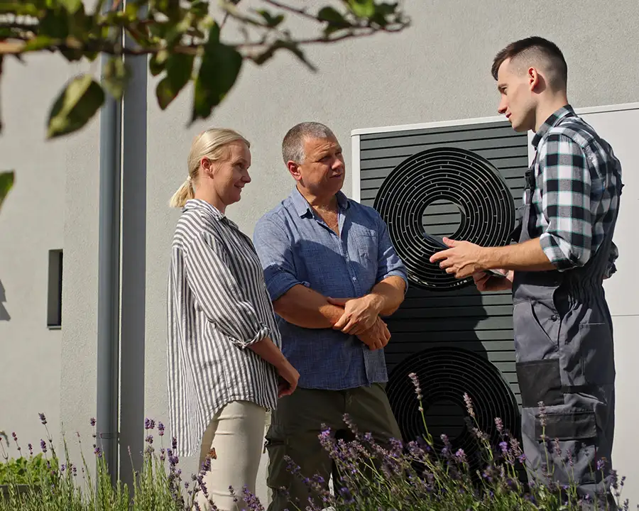 A Precision Climate Control technician explains a newly installed outdoor heat pump unit to an attentive couple in their landscaped backyard in St. Charles, MO
