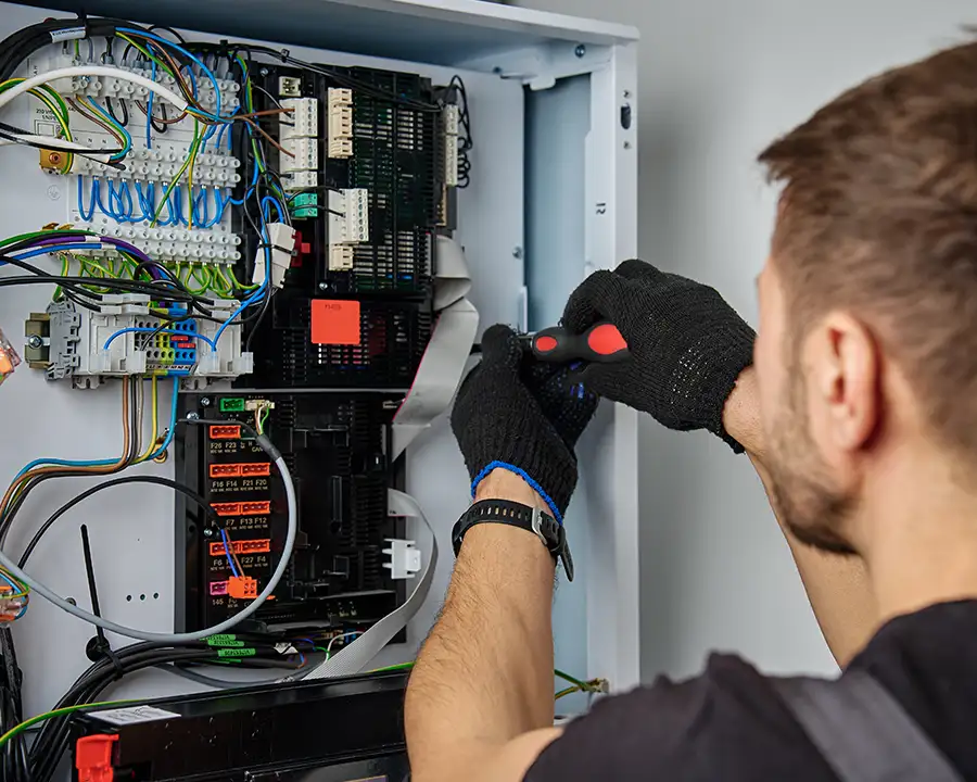 A Precision Climate Control technician wearing black gloves uses a screwdriver for Electric Heating System Installation & Repair in St. Charles, MO