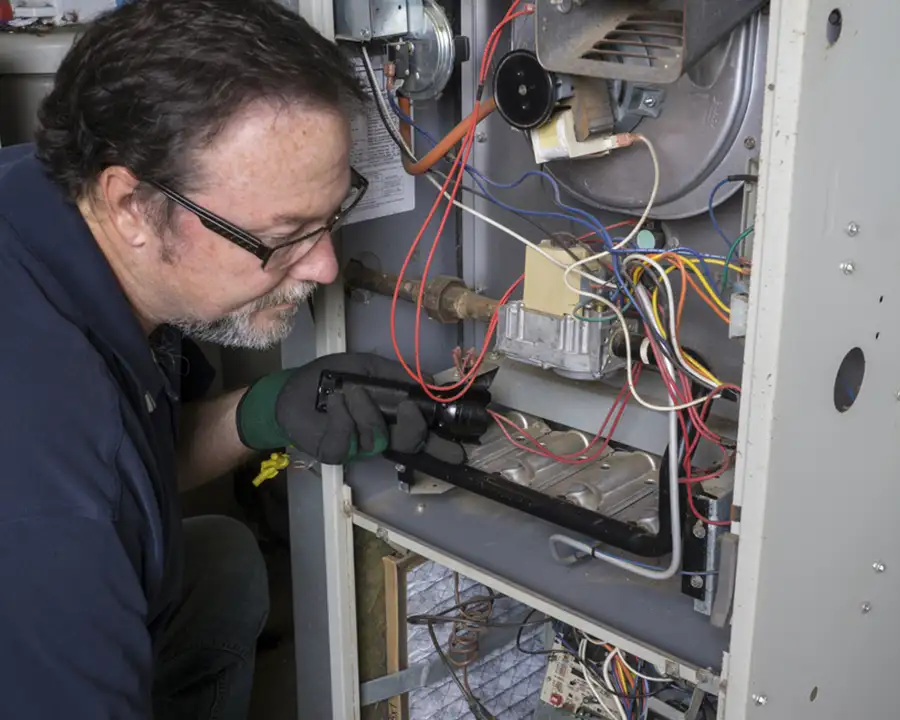 A Precision Climate Control technician in a blue uniform performs Combustion Analysis & Safety Testing to the internal valves, wiring, and gauges of a residential furnace in St. Charles, MO