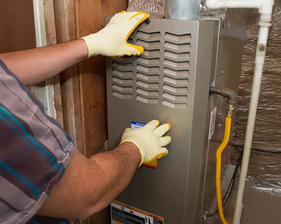 A Precision Climate Control technician wearing safety glasses and red gloves carefully installs a new furnace unit in home in St. Charles, MO